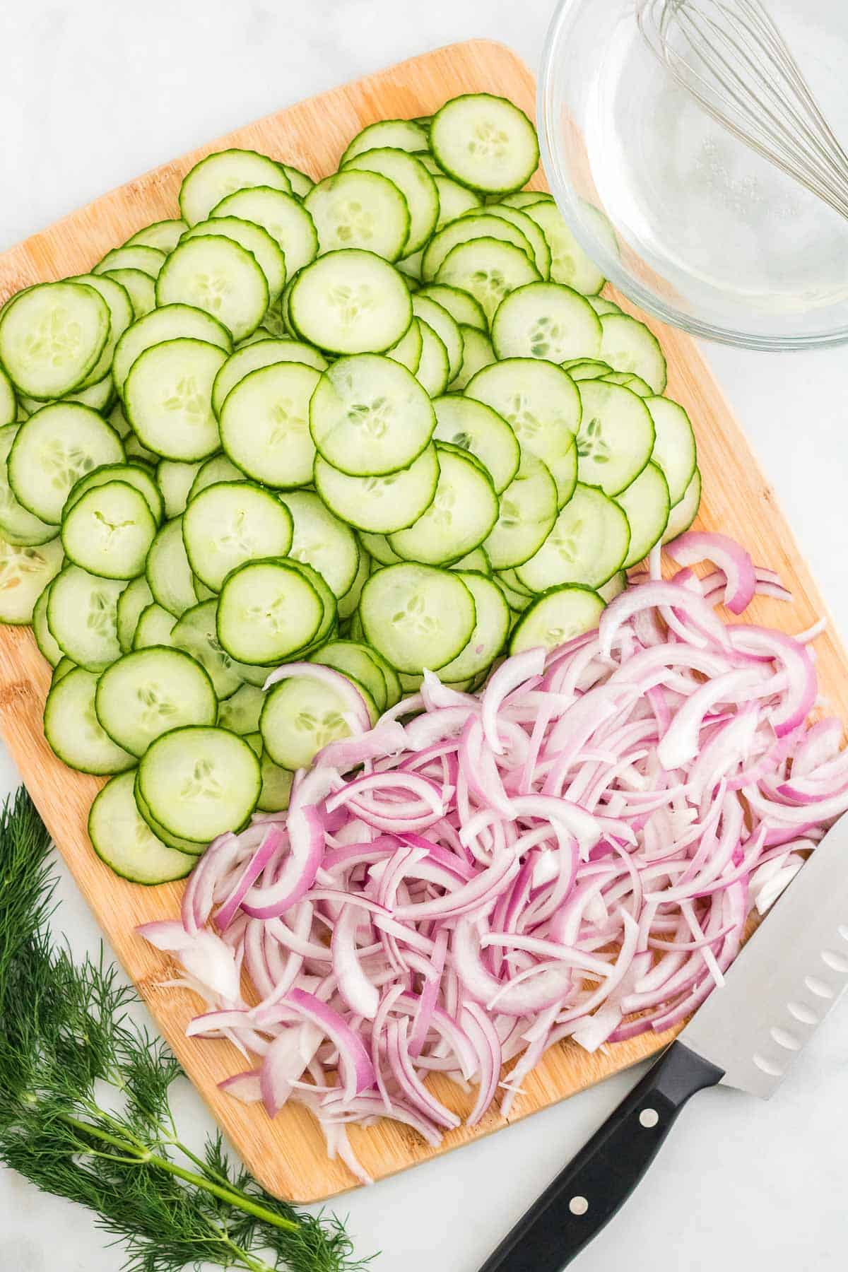 sliced onions and cucumbers on a cutting board.