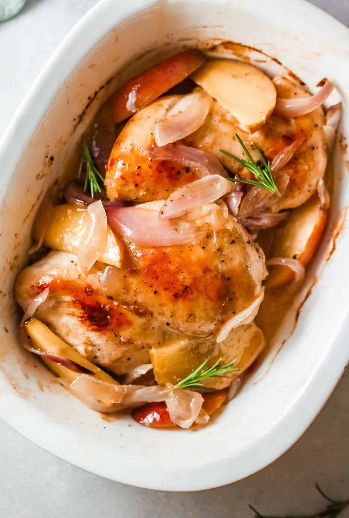 roast chicken with apples and onions in a white baking dish.