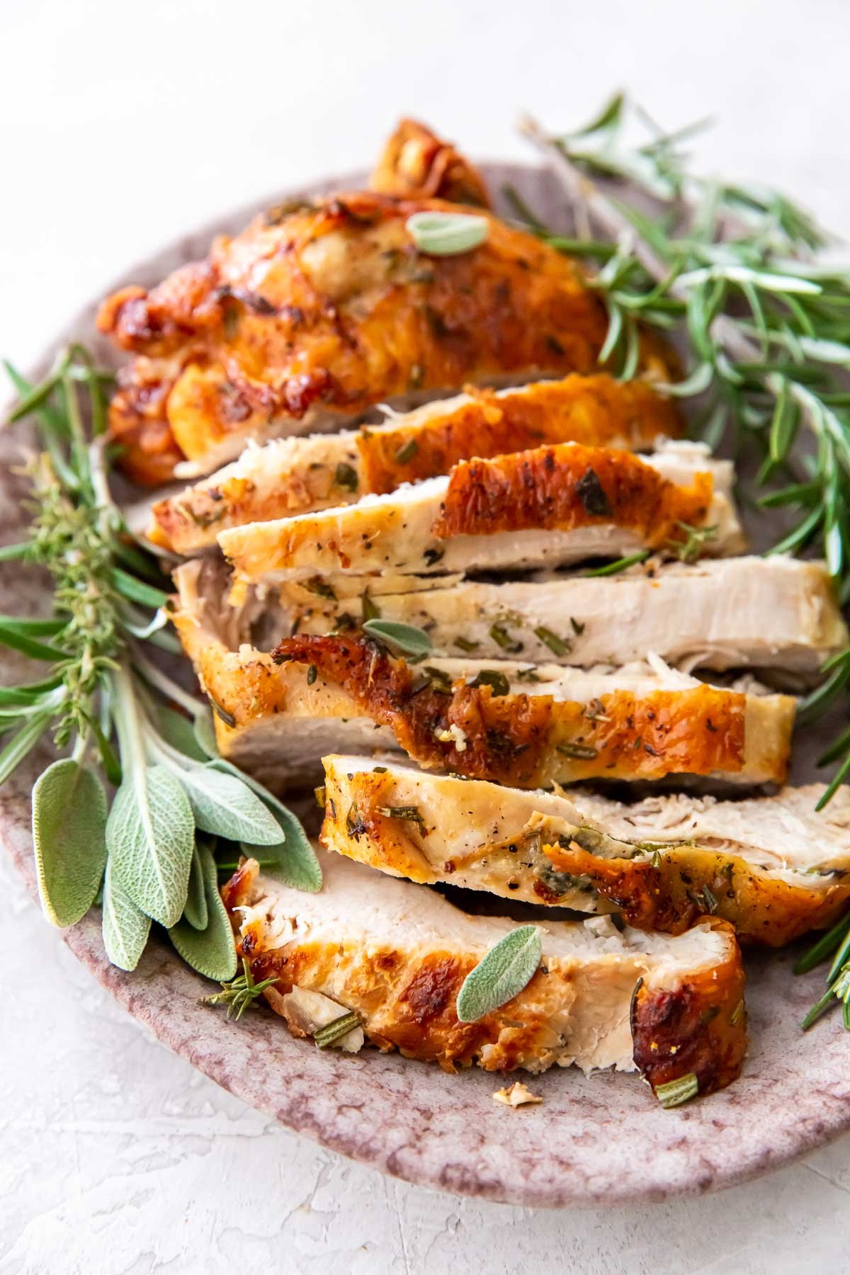 sliced air fryer turkey breast on platter with herbs.