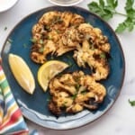 air fryer cauliflower steaks cooked on plate with lemon wedges cropped.