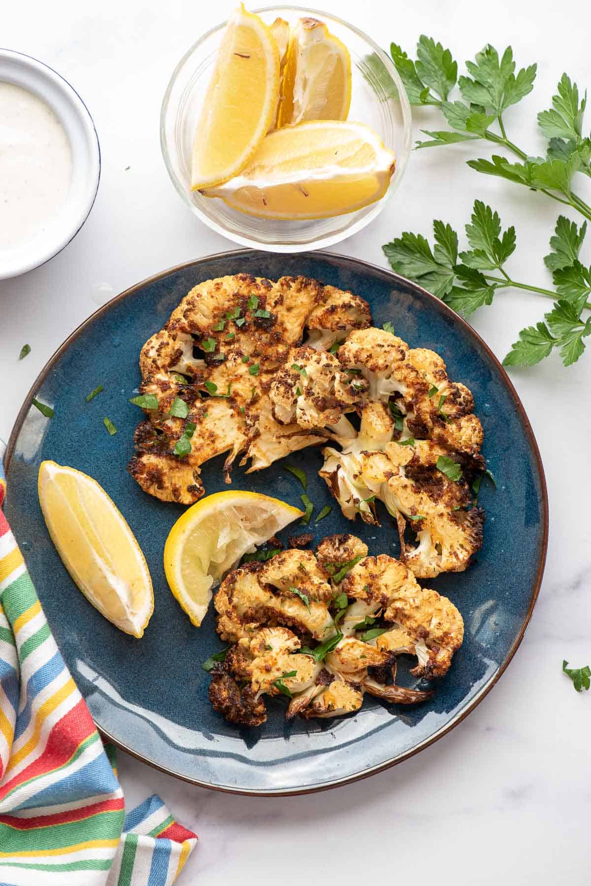 air fryer cauliflower steaks cooked on plate with lemon wedges.