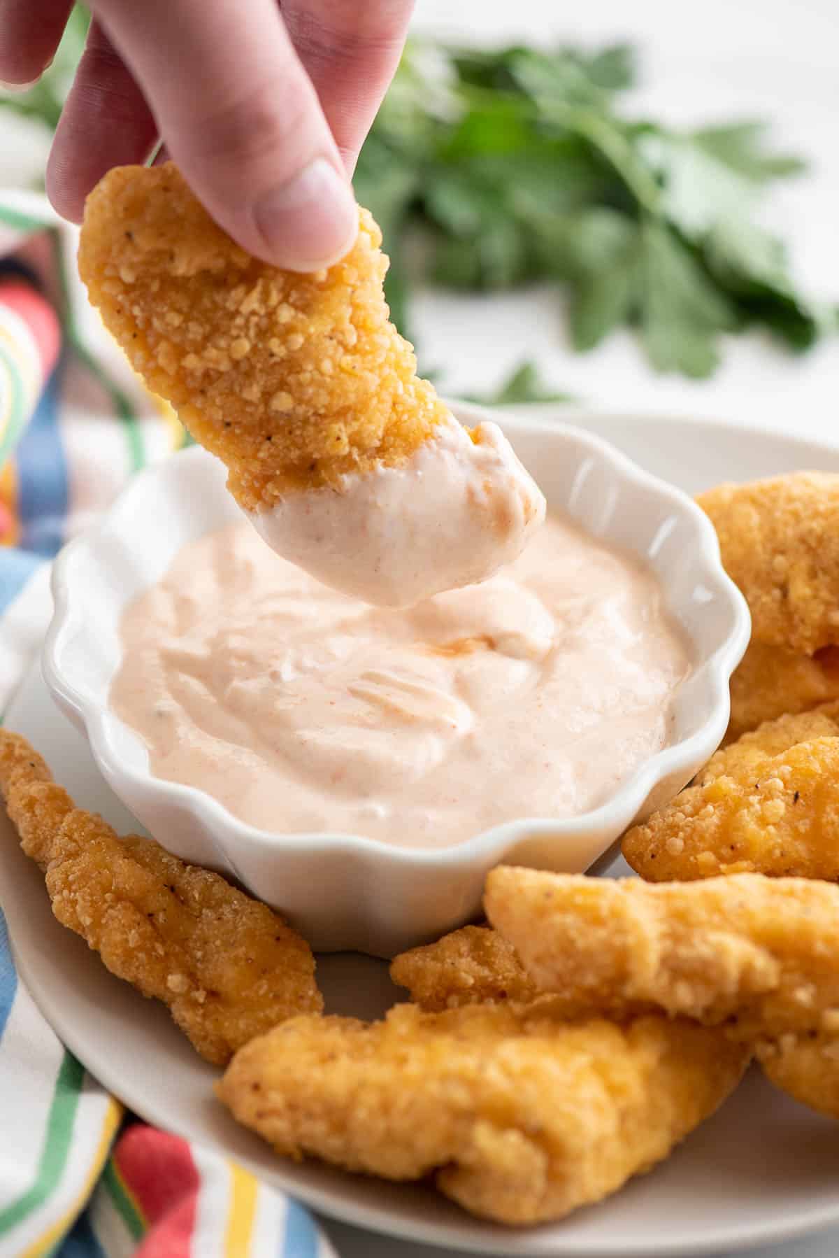 dipping chicken tender in bang bang sauce.